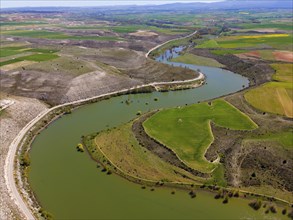 Aerial view of a river winding through a green, hilly landscape with fields, aerial view, near