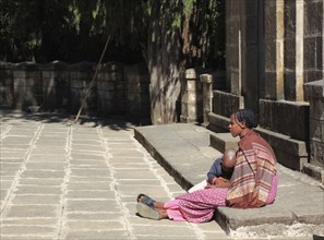 Young African woman with child sitting in front of a house and waiting, Ethiopia, Africa