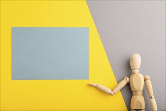 Wooden mannequin holding blue blank poster on gray and yellow pastel background. copy space,