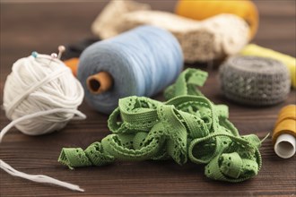 Sewing accessories: scissors, thread, thimbles, braid on brown wooden background. Side view, close