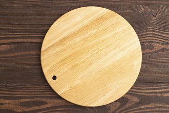 Empty round wooden cutting board on brown wooden background. Top view, flat lay