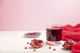 Glass of pomegranate juice on a white and pink background with red textile. Side view, copy space,