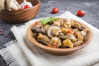 Fried oyster mushrooms with tomatoes in wooden plate on black concrete background. side view, close