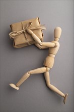 Wooden mannequin holding a gift box on gray pastel background. close up, isolated, delivery concept