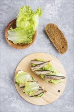 Sprats sandwiches with lettuce and cream cheese on wooden board on a gray concrete background. top