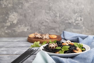 Black cuttlefish ink pasta with shrimps or prawns and small octopuses on gray wooden background and