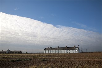 Frontal clouds passing over Coastguard Cottages shingle beach at Shingle Street, Suffolk, England,