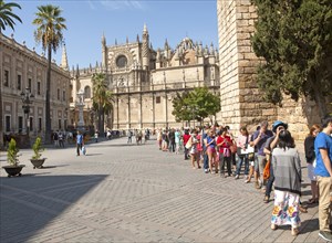 Line of tourists queueing to enter the Alcazar in Seville, Spain with the cathedral in background