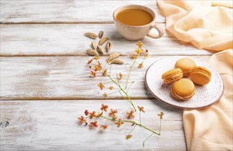 Orange macarons or macaroons cakes with cup of apricot juice on a white wooden background and