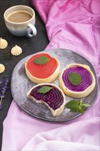 Sweet tartlets with jelly and milk cream with cup of coffee on a black concrete background and pink