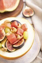 Vegetarian fruit salad of watermelon, grapes, figs, pear, orange, cashew on white wooden background