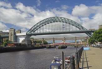 Several bridges over a river in a city, flanked by buildings and boats on a sunny day under a blue