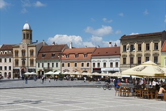 Lively market square with people and cafés, historic facades and parasols in sunny weather, Church