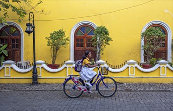 Street scene with girl on bicycle in front of yellow house, Fort Kochi, Cochin, Kerala, India, Asia