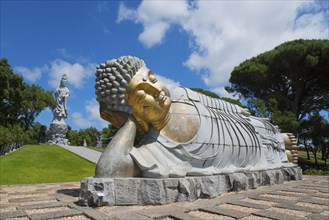 Monumental reclining Buddha statue in a green and peaceful park under a clear blue sky, Bacalhôa,