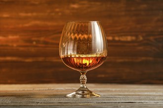 Round shiny glass filled with brandy or cognac, amber liquid on blurred wooden background