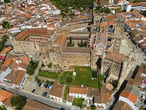 Aerial view of an old monastery with courtyard and red roofs, surrounded by a village in Spain.