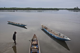 Boatman and pirogues, estuary and mangrove in the background (Fadiouth, Senegal)