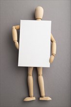 Wooden mannequin holding blank poster on gray pastel background. copy space, isolated, presentation