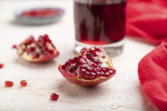 Glass of pomegranate juice on a white concrete background with red textile. Side view, close up,