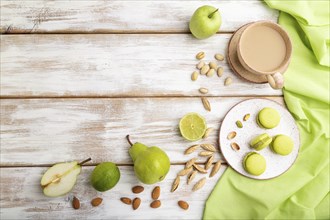 Green macarons or macaroons cakes with cup of coffee on a white wooden background and green linen