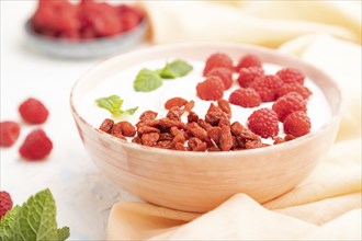 Yogurt with raspberry and goji berries in ceramic bowl on white concrete background and orange