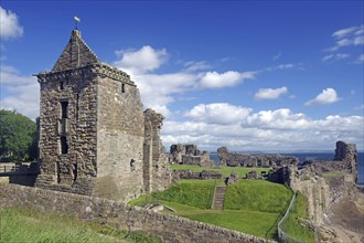 Historic castle ruins with stone tower on a grassy hill under a blue sky, St Andrews, Scotland,