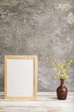 Wooden frame with yellow barrenwort flowers in ceramic vase on gray concrete background. side view,