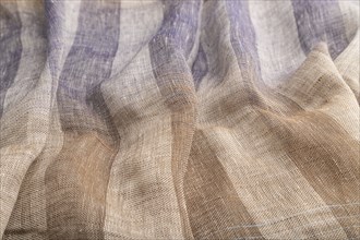 Fragment of brown and violet linen tissue. Side view, natural textile background and texture. wave