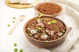 Quinoa porridge with green pea and chicken in wooden bowl on a white wooden background and linen