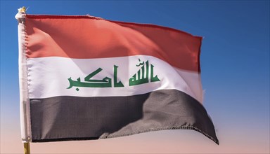 The flag of Iraq flutters in the wind, isolated against a blue sky