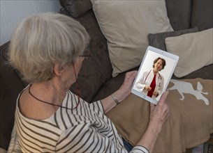 Symbolic image of telemedicine, patient speaking to a doctor in a video conference from home