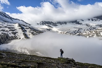 Mountaineer photographed, in front of mountain landscape, high fog in the valley, glaciated