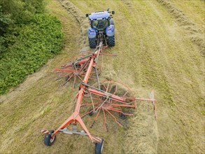 Aerial view of a tractor with hay machine in a field, surrounded by cut grass and hay bales,