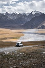 Off-road vehicle on a gravel track, glaciated and snow-covered peaks, Ak Shyrak Mountains, near