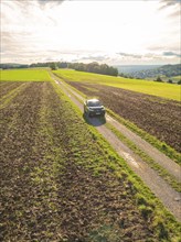 A car on a country road between wide fields under a sky with evening sunlight, car sharing, VW ID5,