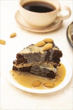 Pieces of chocolate brownie cake with caramel cream and almonds on a white concrete background.