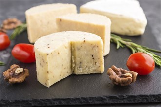 Cheddar cheese and various types of cheese with rosemary and tomatoes on black slate board on a