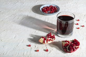 Glass of pomegranate juice on a white concrete background. Hard light, contrast. Side view, copy