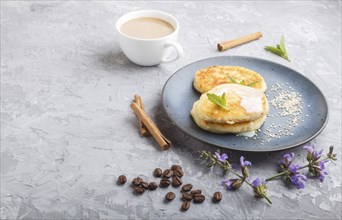 Cheese pancakes on a blue ceramic plate and a cup of coffee on a gray concrete background. side