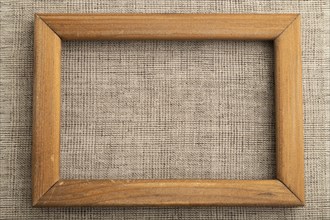 Wooden frame on smooth brown linen tissue. Top view, flat lay, natural textile background and