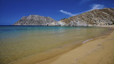 Natural beach with turquoise waters and a picturesque mountain backdrop under a clear sky, Psili