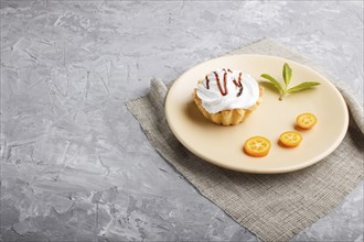 Cake with whipped egg cream on a light brown plate with kumquat slices and mint leaves on a gray