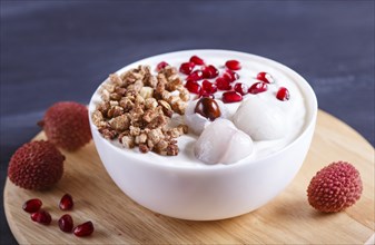 Greek yogurt with lychee, pomegranate seeds and granola in a white plate on a black wooden