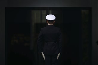 A marine stands with his back to the camera in front of the entrance to the Federal Chancellery.