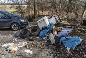 Illegal waste disposal in a car park, in a wooded area, tyres, furniture, refrigerators, household