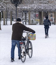 Winter in the city, cyclist pushes his bike over the closed snow cover in front of the opera,