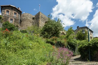 Historic village of Auzon with overgrown greenery under a bright blue sky, Haute-Loire,