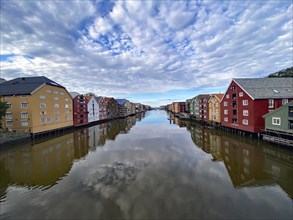 River reflecting colourful wooden buildings under a cloudy blue sky, calm atmosphere, view from the