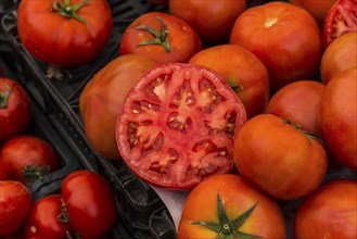 Close-up of fresh red tomatoes, one of them cut open, the others in the background, market stall,